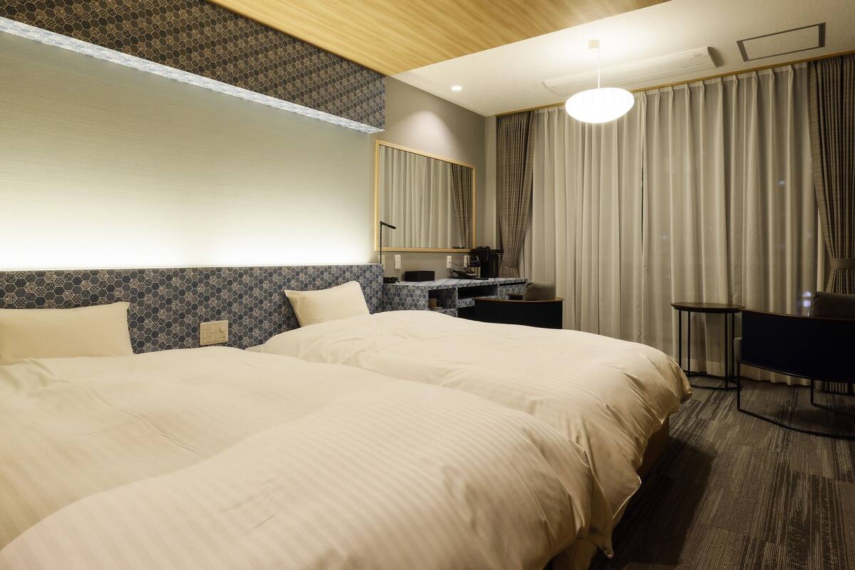 A hotel room with two large beds, a desk, a chair, a mirror, and a window with curtains.