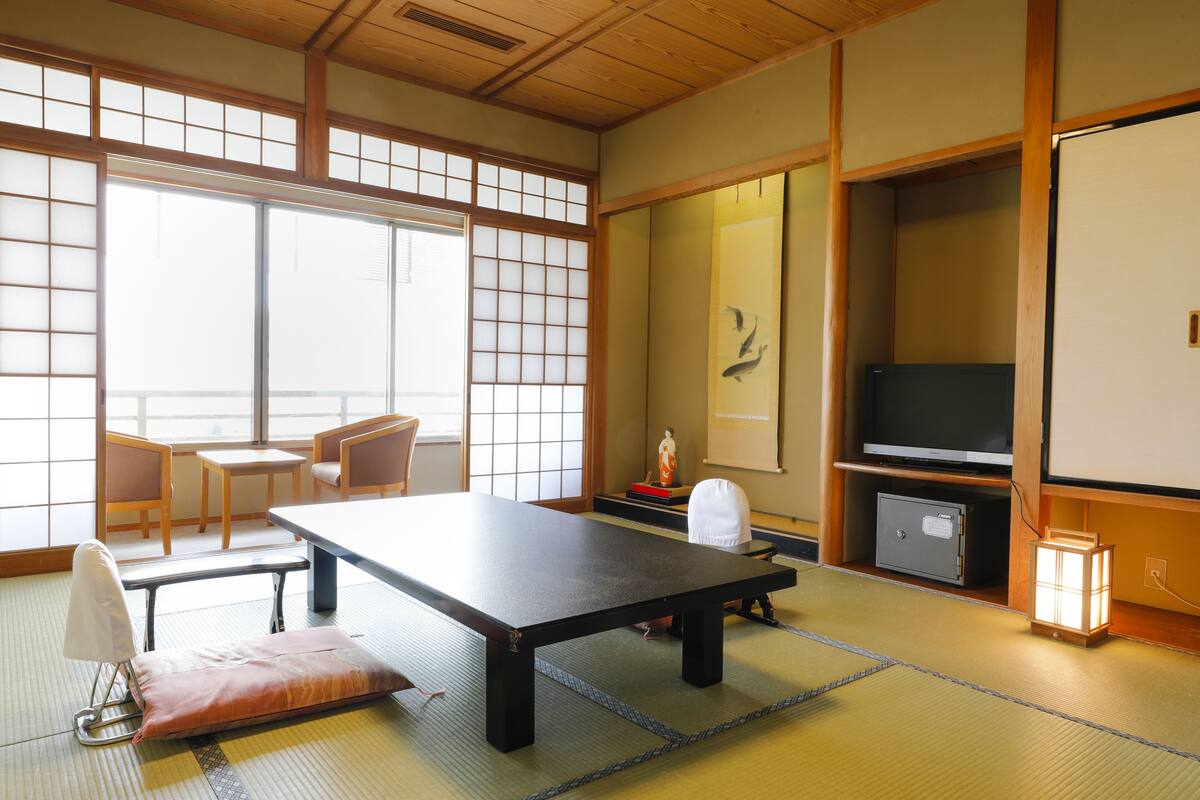 A traditional Japanese room with tatami flooring, a low table, chairs, a television, and a cabinet.