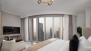 A modern hotel room with a large bed, a flat-screen TV, a sofa, and a view of the cityscape through large windows. -  Maison Privee - Ultra Chic High-Floor Apt w/ Direct Burj Khalifa & Fountains Views (Dubai)