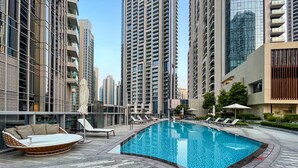A rooftop swimming pool with lounge chairs and a sunbed, surrounded by high-rise buildings. -  Maison Privee - Ultra Chic High-Floor Apt w/ Direct Burj Khalifa & Fountains Views (Dubai)