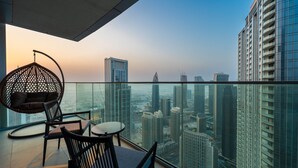 A balcony with a city view, a hanging chair, and a small table. -  Maison Privee - Ultra Chic High-Floor Apt w/ Direct Burj Khalifa & Fountains Views (Dubai)
