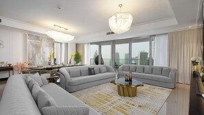 A modern living room with a sectional sofa, a coffee table, and a large window with a city view. -  Maison Privee - Ultra Chic High-Floor Apt w/ Direct Burj Khalifa & Fountains Views (Dubai)