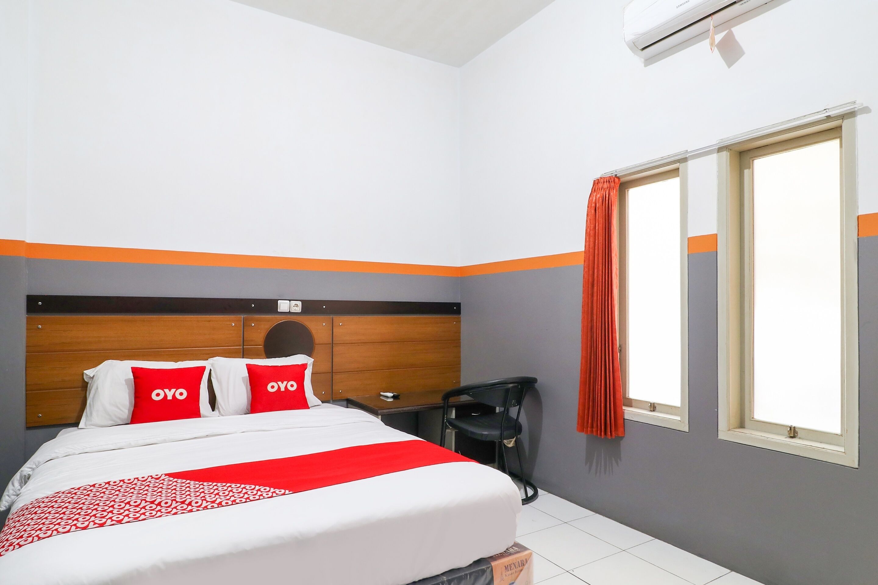 Una habitación de hotel con cama, mesita de noche, una silla y una ventana con cortinas.