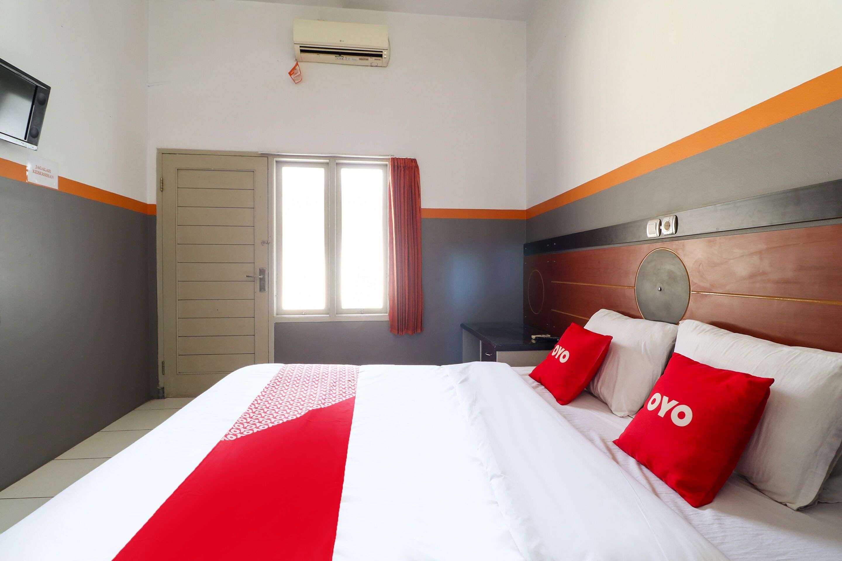 A hotel room with a bed, a television, an air conditioner, and a window with curtains.