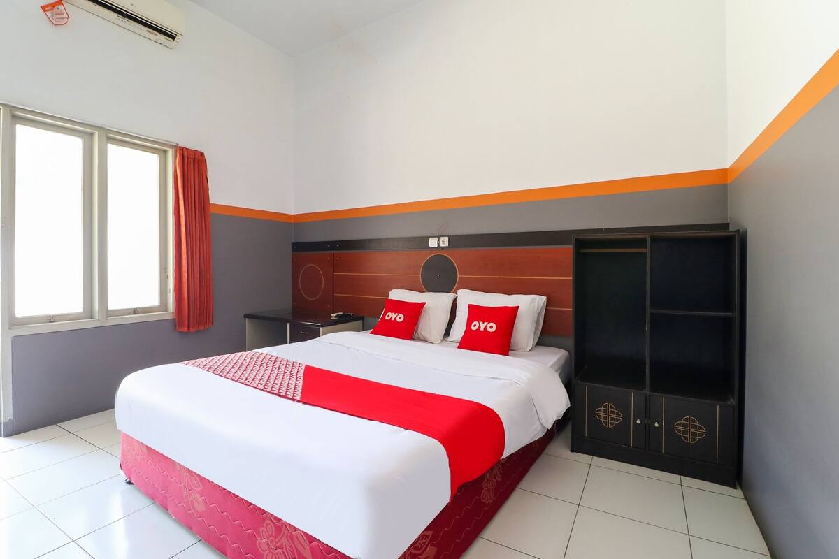 Une chambre d’hôtel avec un grand lit, une armoire et une fenêtre avec des rideaux.