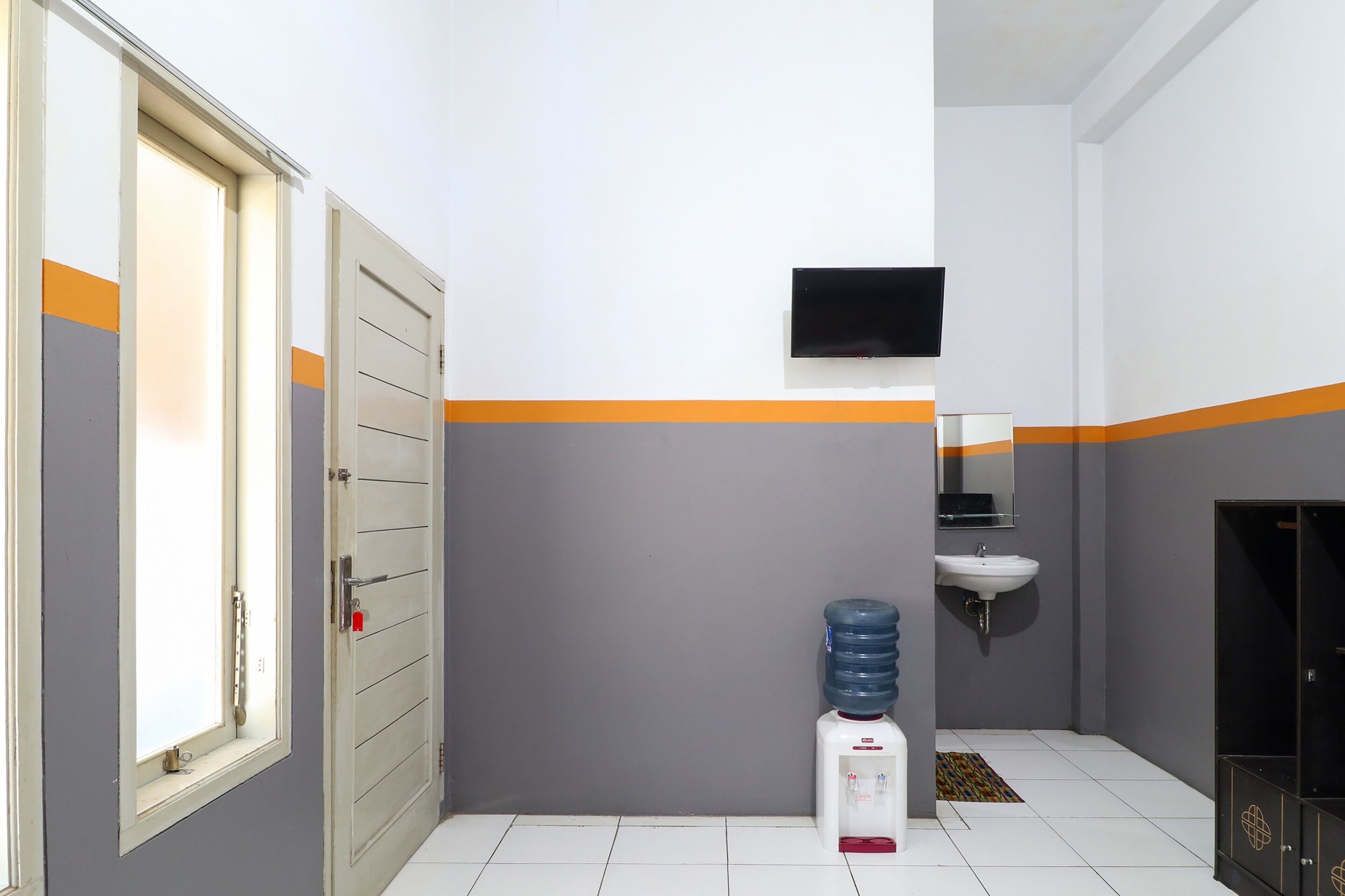 A bathroom with a water dispenser, a sink, and a television mounted on the wall.