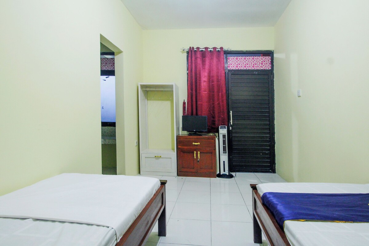 Una habitación con dos camas, un televisor sobre un soporte y una puerta cerrada.