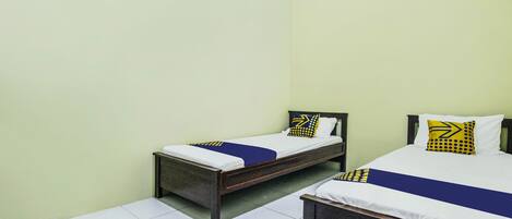 A room with two single beds, each with a wooden frame and white bedding. The walls are painted light green, and the floor is tiled with white tiles.