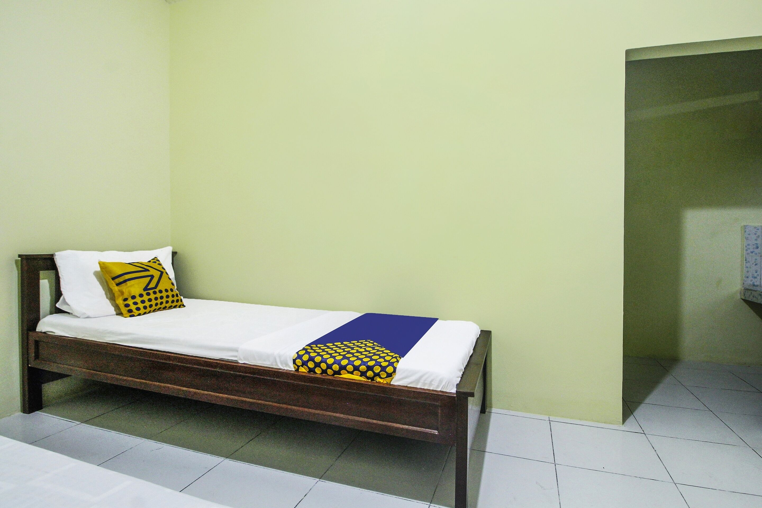 A single bed with a wooden frame, white bedding, and a yellow and blue pillow.