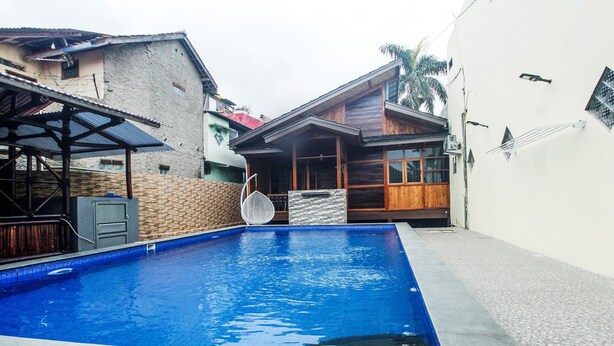 A rectangular swimming pool with a tiled edge, surrounded by a brick wall and a wooden deck. - OYO Life 91606 Nadin Guest House Syariah (Garut)