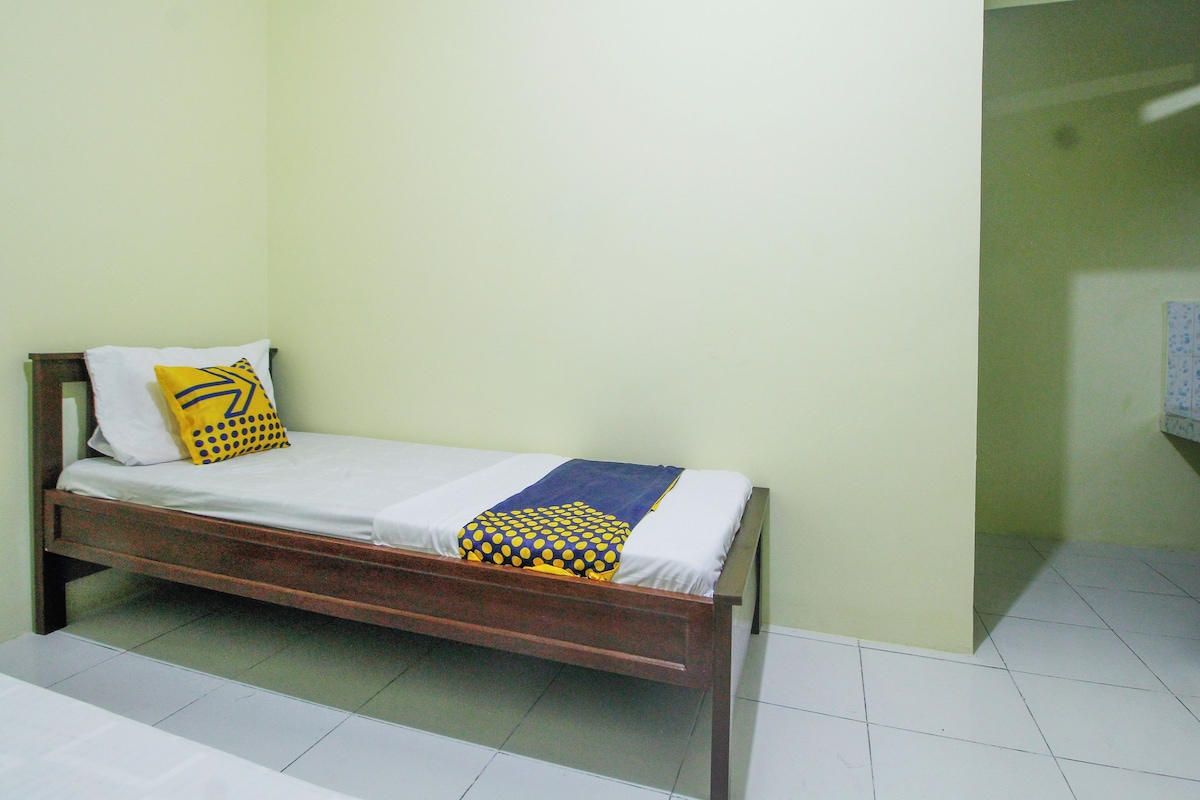 A single bed with a wooden frame, white bedding, and two pillows, one with a yellow pattern.