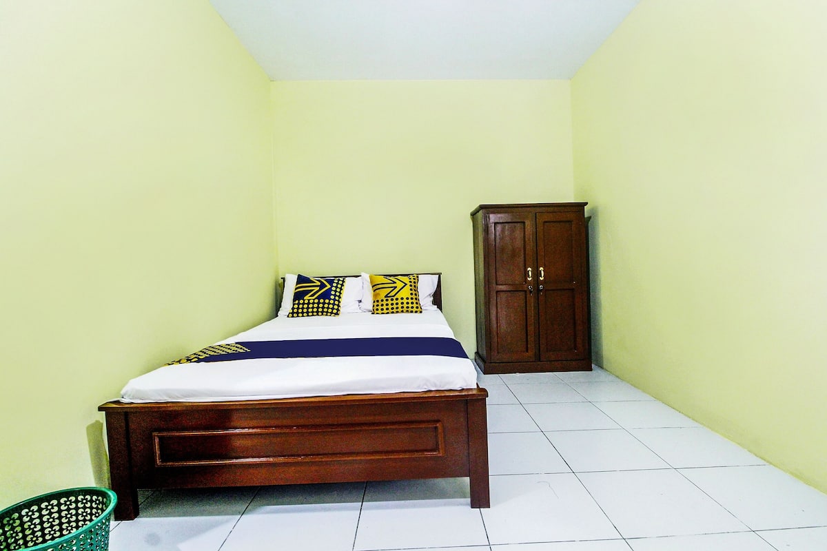 Une petite chambre à coucher, bien rangée, avec un lit en bois, un panier vert et une armoire en bois.