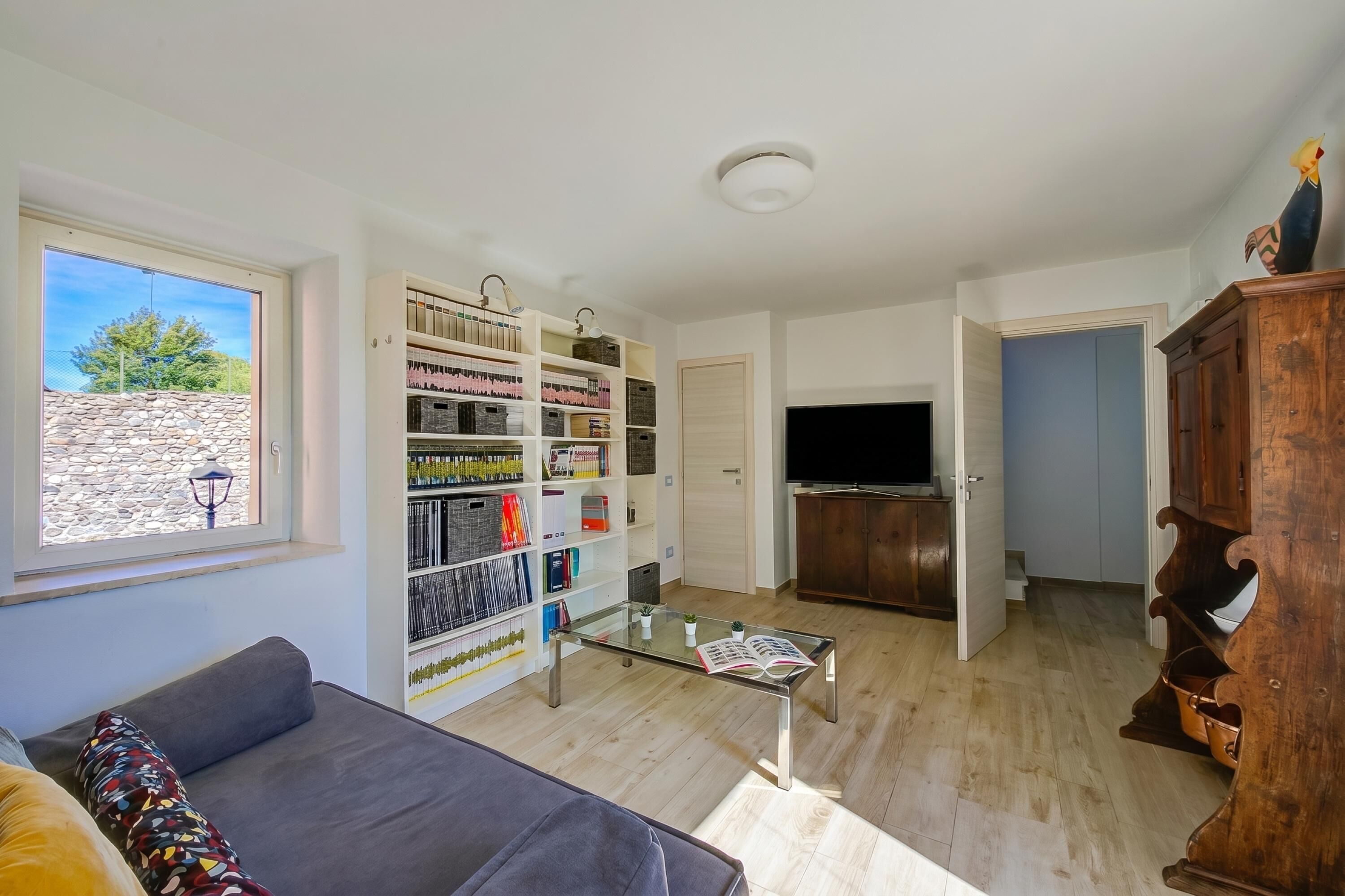 A living room with a sofa, a glass-top coffee table, a bookshelf, a television, and a wooden cabinet.