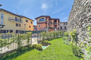 Una zona residencial con un muro de piedra, un patio cubierto de césped y edificios con balcones y ventanas.