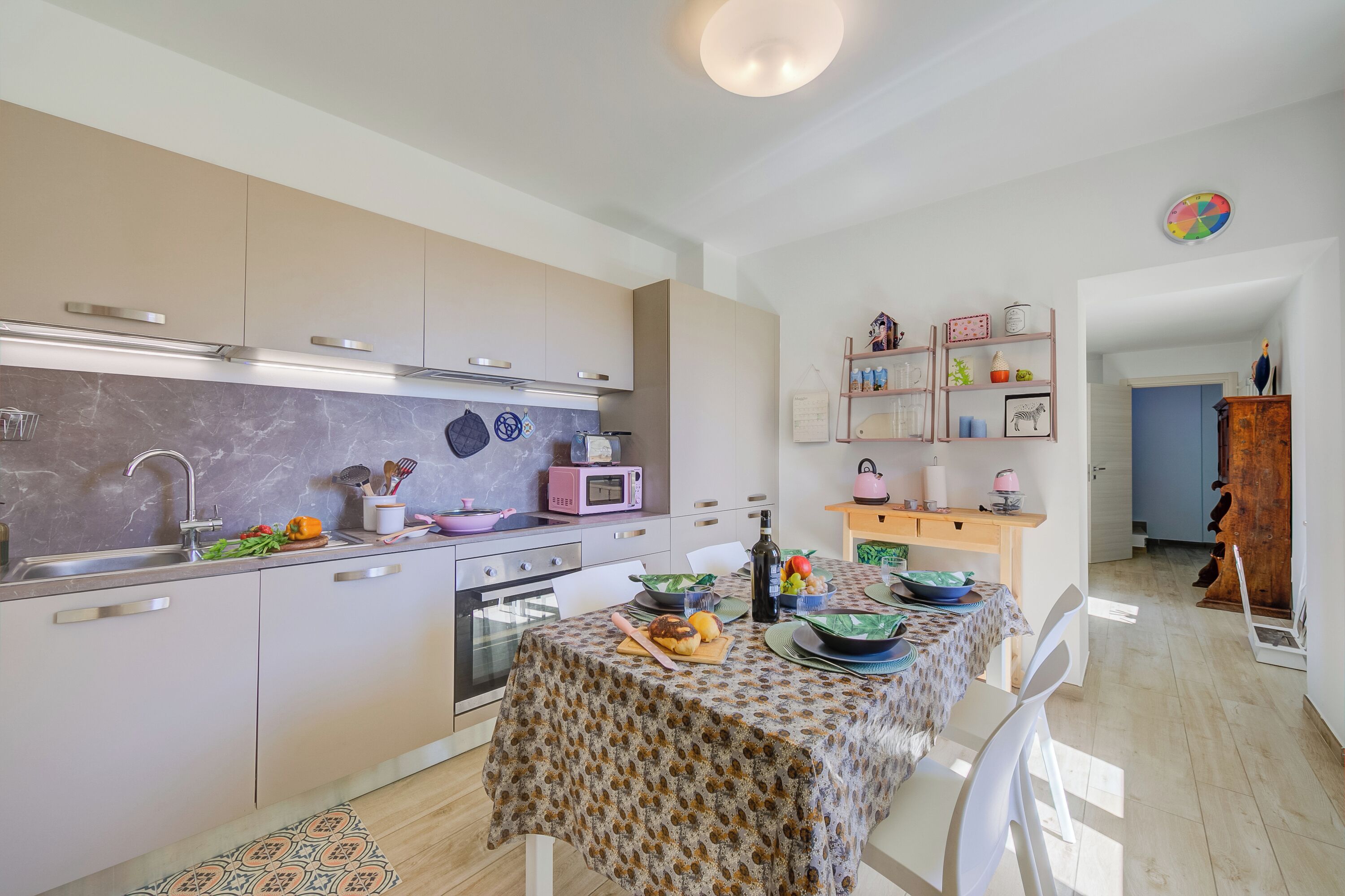 Een moderne keuken met een marmeren aanrechtblad, roestvrijstalen apparatuur en een eethoek met een tafelkleed met dessin.