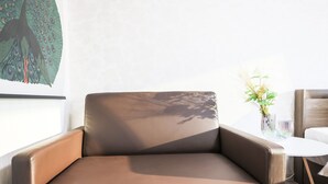 Moderni huone, jossa on ruskea nahkasohva, valkoinen pyöreä pöytä ja seinälle ripustettu taulu, jossa on kuvattuna riikinkukko.