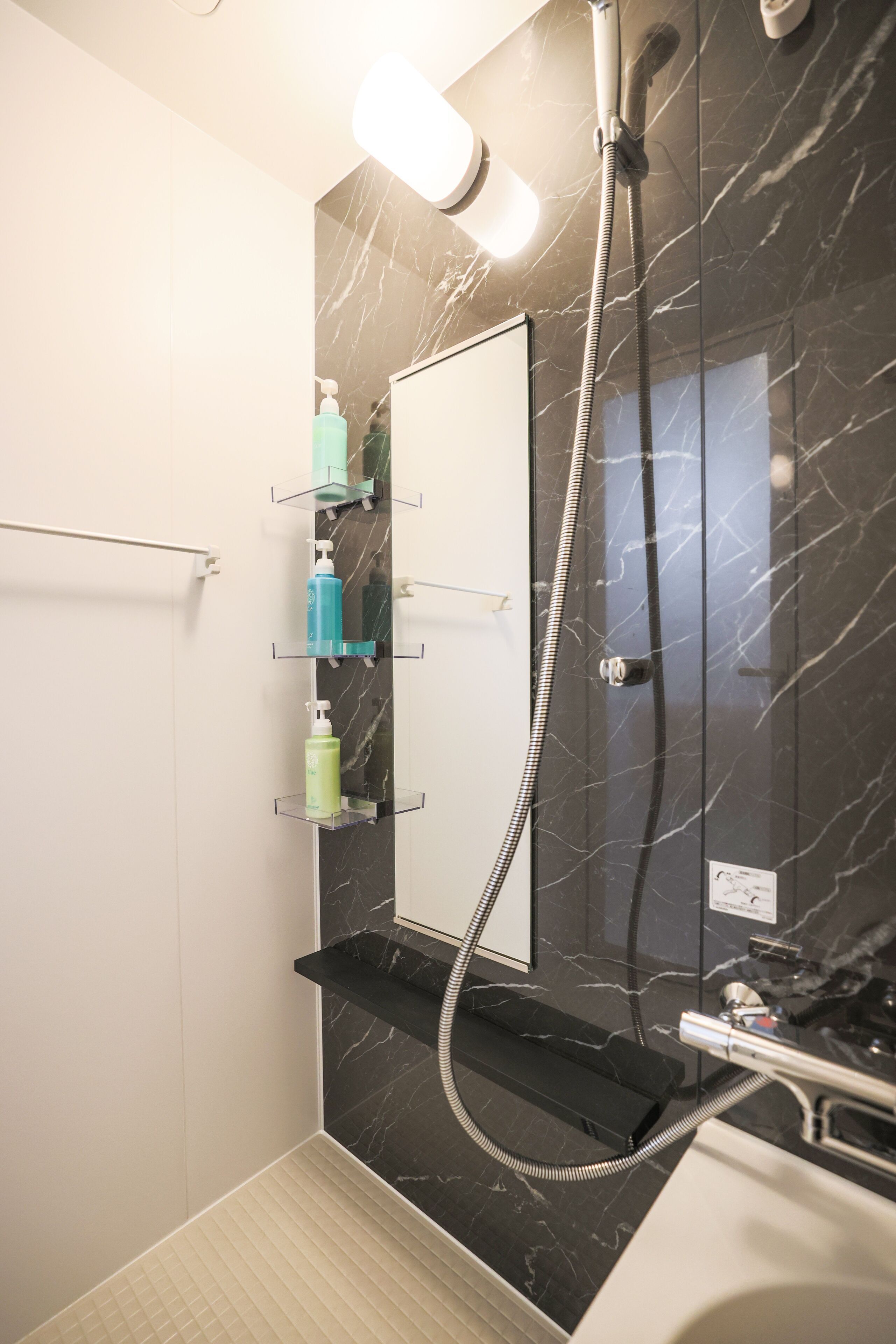 Een moderne badkamer met een marmeren wand, een inbouwspiegel en een douche met handdouche.