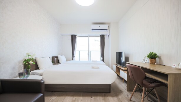Moderni hotellihuone, jossa on suuri sänky, työpöytä, tuoli, televisio ja ruukussa oleva kasvi.