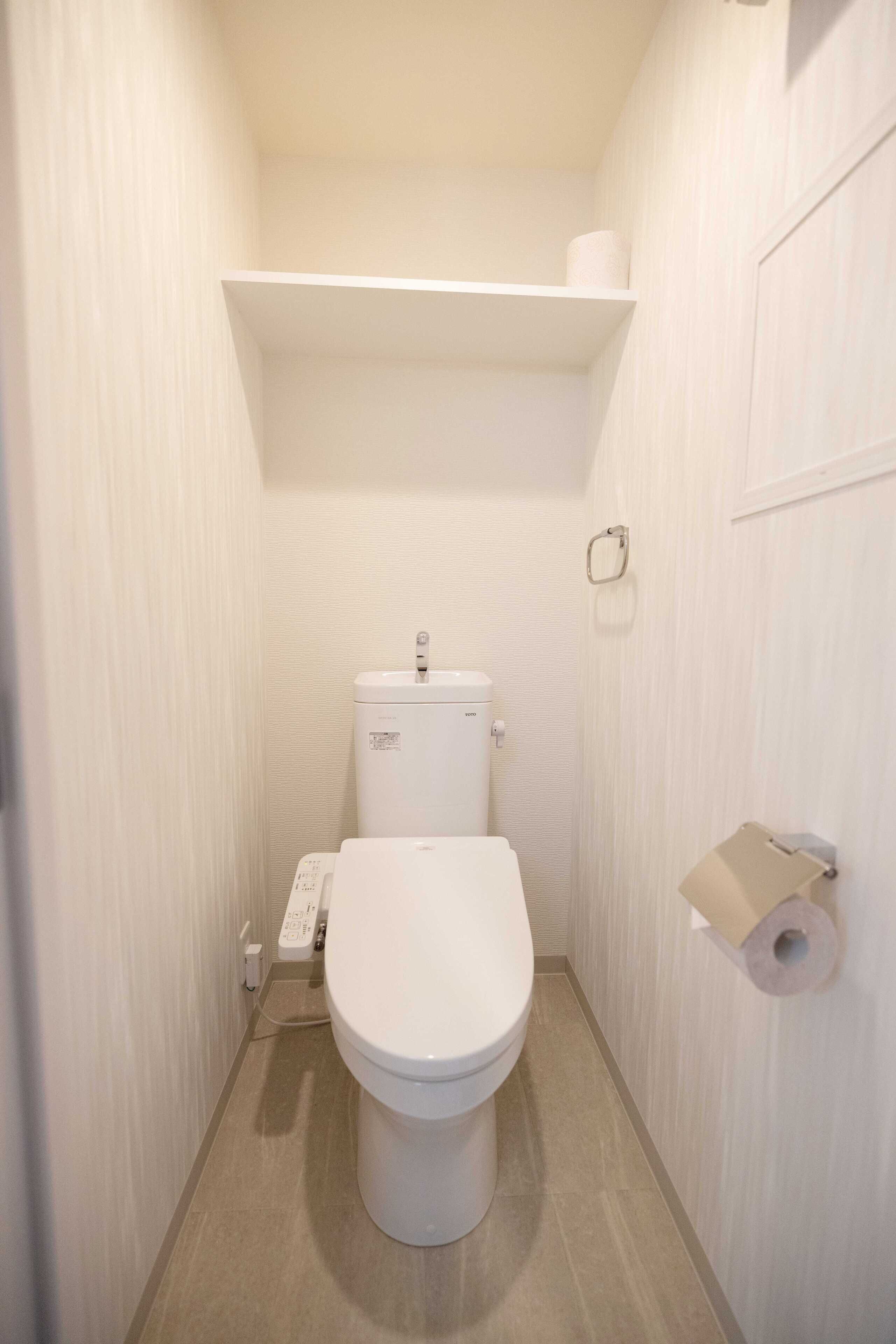 A small, narrow bathroom with a toilet, a sink, and a toilet paper holder.