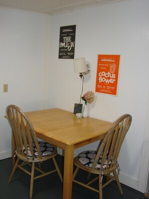 Un comedor con una mesa de madera y dos sillas, una lámpara de pared y dos carteles anunciando eventos.