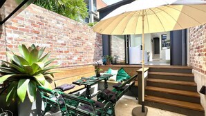 Un patio con pared de ladrillo, escalera de madera y mobiliario exterior.