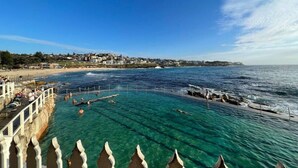 A coastal view with clear waters, a pier, and a town in the background. - Paddington Dream - an Urban Oasis (Paddington)