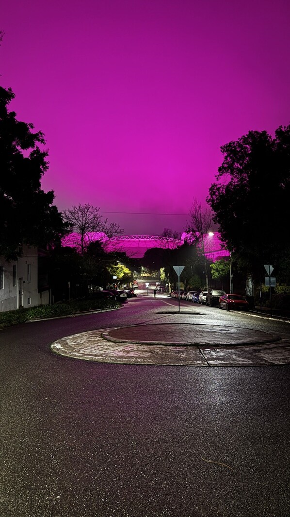 A street at night with a purple sky, a roundabout, and a bridge in the distance.