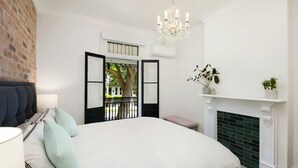 A bedroom with a large bed, a chandelier, a fireplace, and a view of the outside. - Paddington Dream - an Urban Oasis (Paddington)