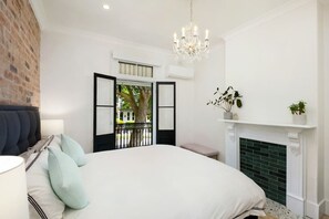 A bedroom with a large bed, a chandelier, a fireplace, and a view of the outdoors. - Paddington Dream - an Urban Oasis (Paddington)