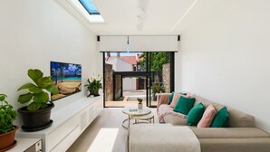 A modern living room with a sofa, a coffee table, and a view of the outside. There are potted plants and a painting on the wall. - Paddington Dream - an Urban Oasis (Paddington)