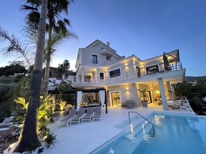 Una casa de dos pisos con piscina, mobiliario exterior y un balcón.