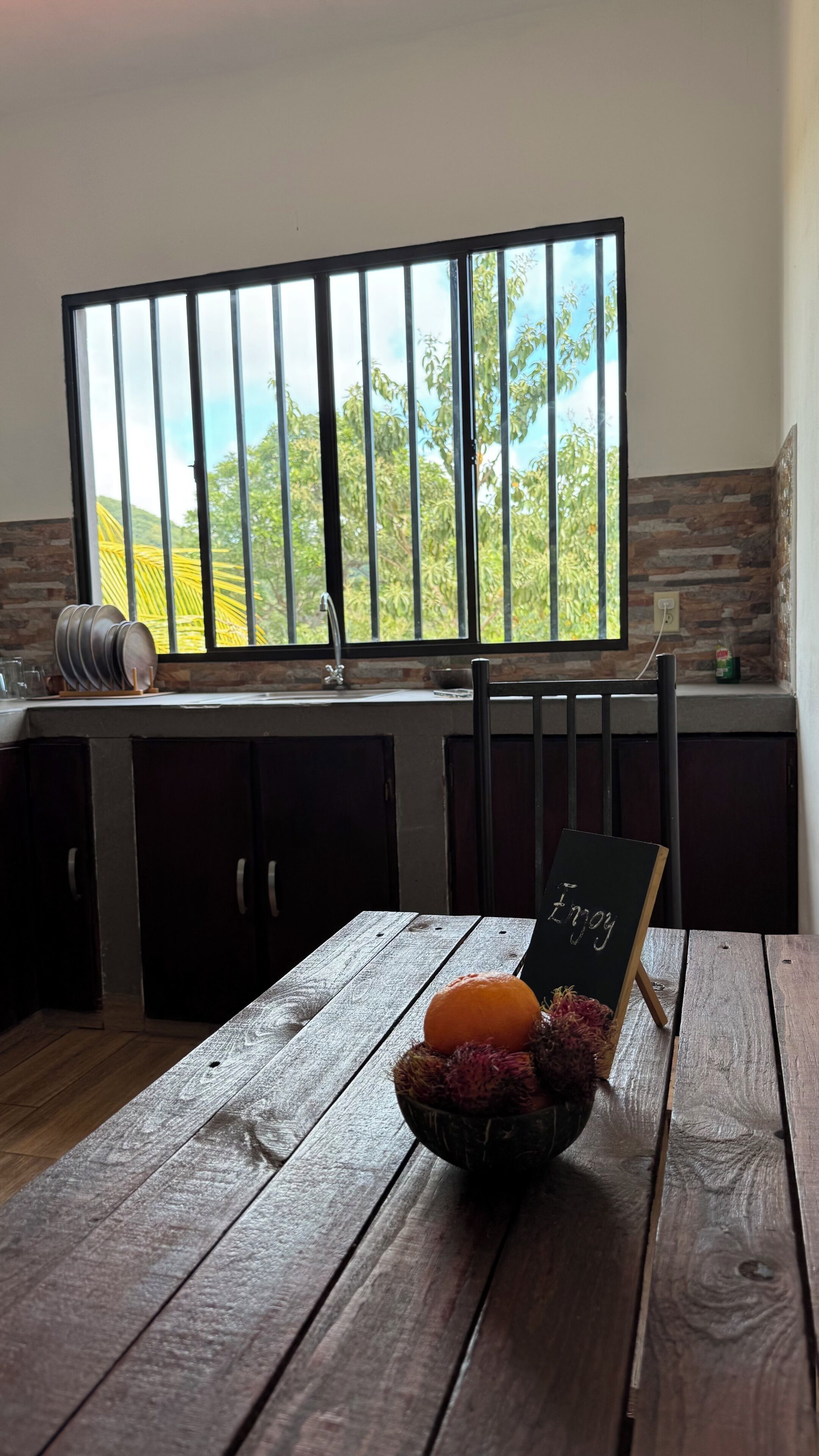 A kitchen with a window, a wooden table, and a bowl of fruit.