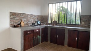 A kitchen with a stone backsplash, a window with a view of greenery, and wooden cabinets. - Casa Melodía 🌿 2BR Near El Cuco & Las Flores (Chirilagua)