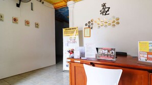 A reception desk with a wooden finish, a white chair, and various informational signs on the wall, including a no smoking sign and a promotional poster for a local event. - OYO 91607 Steze Guest House Syariah (Jambi)