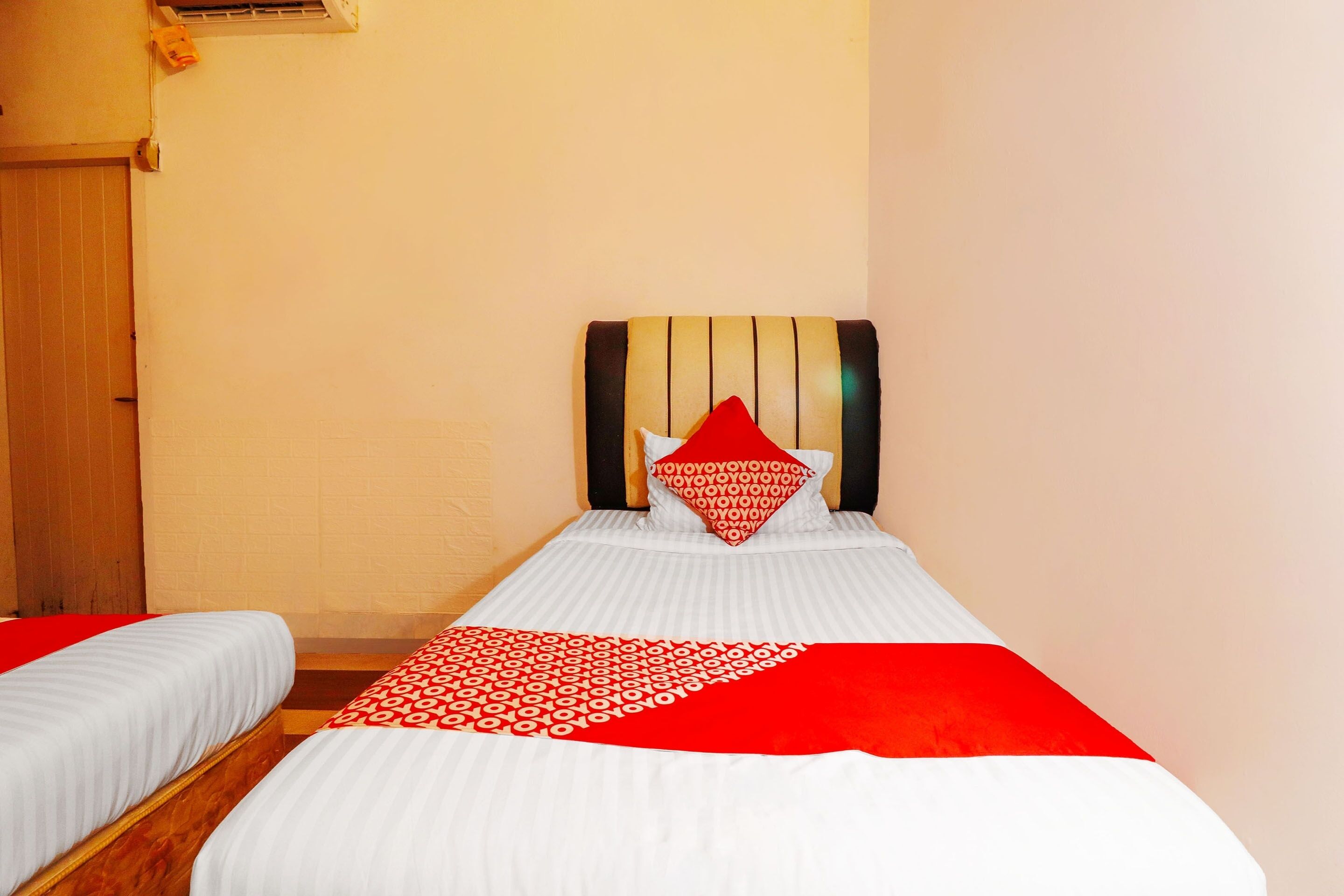 A hotel room with two single beds, a wooden door, and a plain wall.