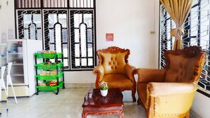 A room with two ornate chairs, a small wooden table with a potted plant, and a green shelf with snacks. - OYO 91607 Steze Guest House Syariah (Jambi)