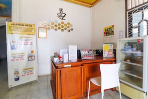 Un espace d’accueil avec un comptoir en bois, une chaise blanche, un réfrigérateur et des affiches promotionnelles accrochées au mur.