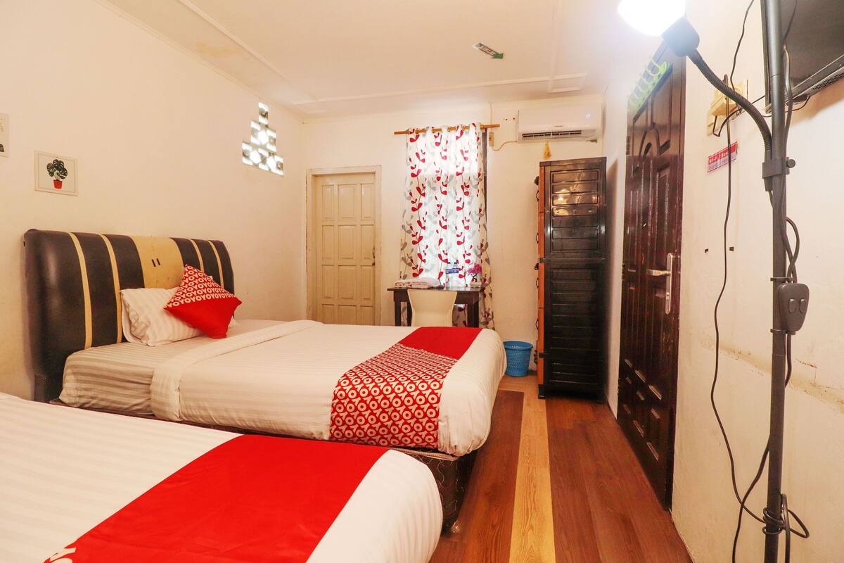 A hotel room with two beds, a desk, a chair, a wardrobe, and a shower area.