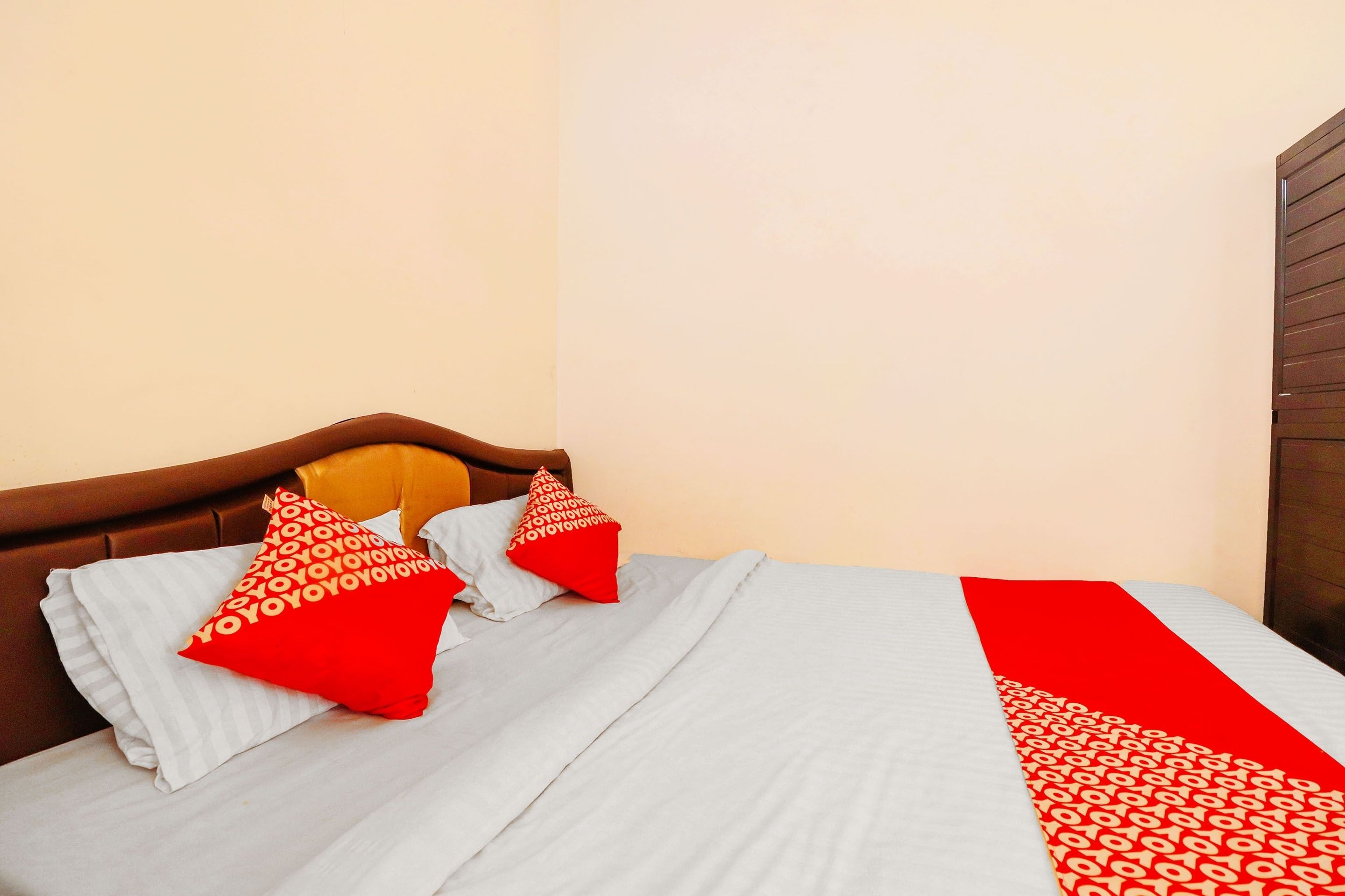 A bed with a white and red bedspread, two red pillows with a pattern, and a wooden headboard.