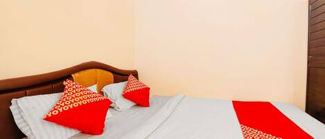 A bed with a white and red bedspread, two red pillows with a pattern, and a wooden headboard.