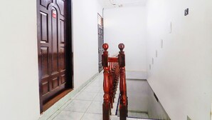 A narrow hallway with a wooden door on the left and a staircase with a balustrade leading to an upper floor. - OYO 91607 Steze Guest House Syariah (Jambi)