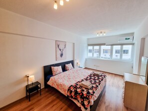 Un dormitorio con una cama, una mesita de noche, una lámpara, una ventana y un aire acondicionado instalado en la pared.