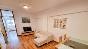 A modern living room with a wooden floor, a beige sofa, a TV on a wooden stand, and a dining table with chairs.