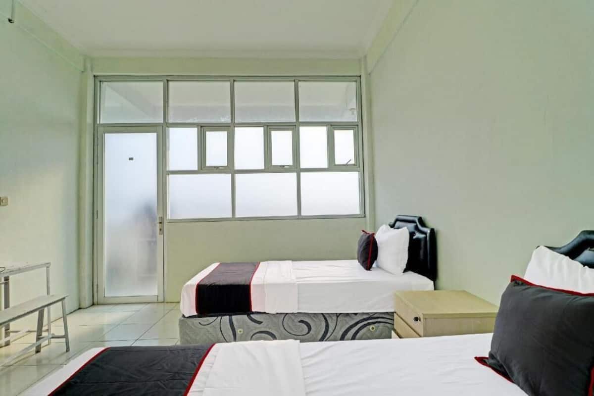 Une chambre d’hôtel avec deux lits, un banc, une fenêtre et une porte.