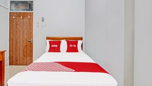 A neatly made bed with a red and white bedspread and pillows, a wooden headboard, and a wooden door with a window above it. - OYO 91960 Fariza House Syariah  (Kendal)