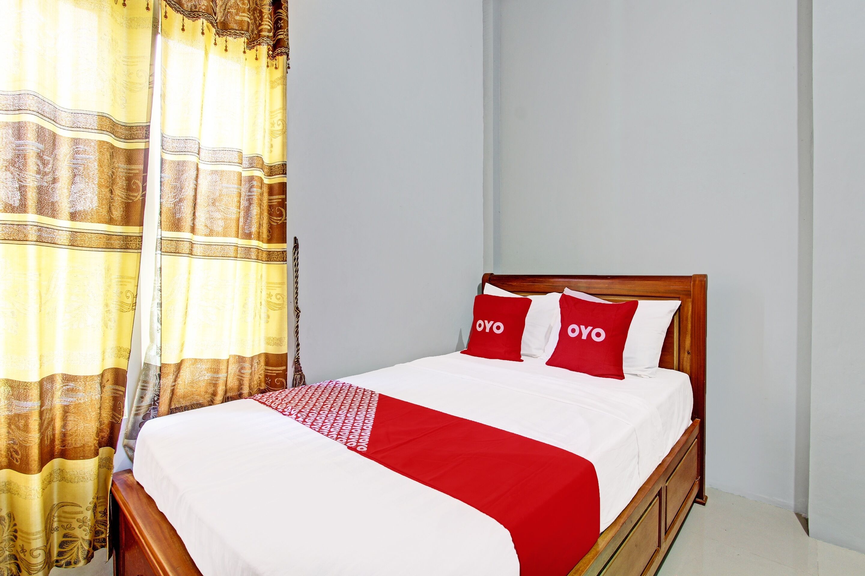 A neatly made bed with a red and white bedspread and two pillows with the word "OYO" on them.