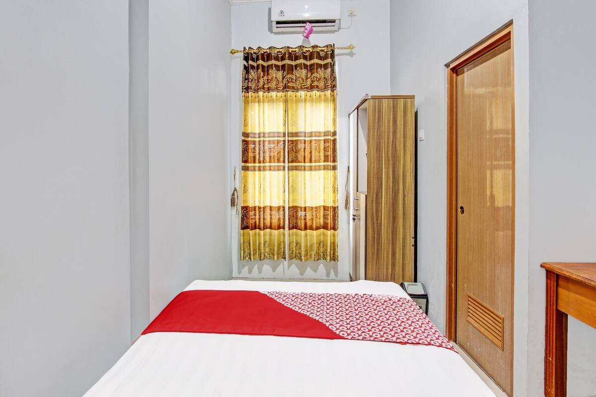 Une chambre d’hôtel avec un lit, une armoire en bois, une porte et un rideau.