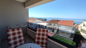 A balcony with a table and chairs, overlooking a coastal town with buildings and a clear sky.
