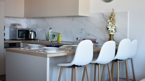 A modern kitchen with a marble backsplash, a microwave, and a dining area with white chairs.