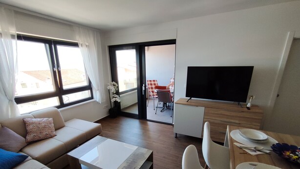 A modern living room with a sofa, coffee table, and dining area with chairs and a TV.